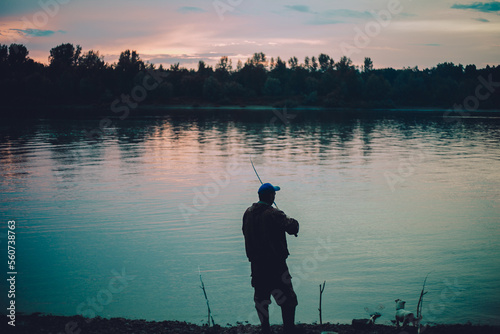 the silhouette of a male fisherman on the shore after sunset. A fisherman throws a fishing rod into the water