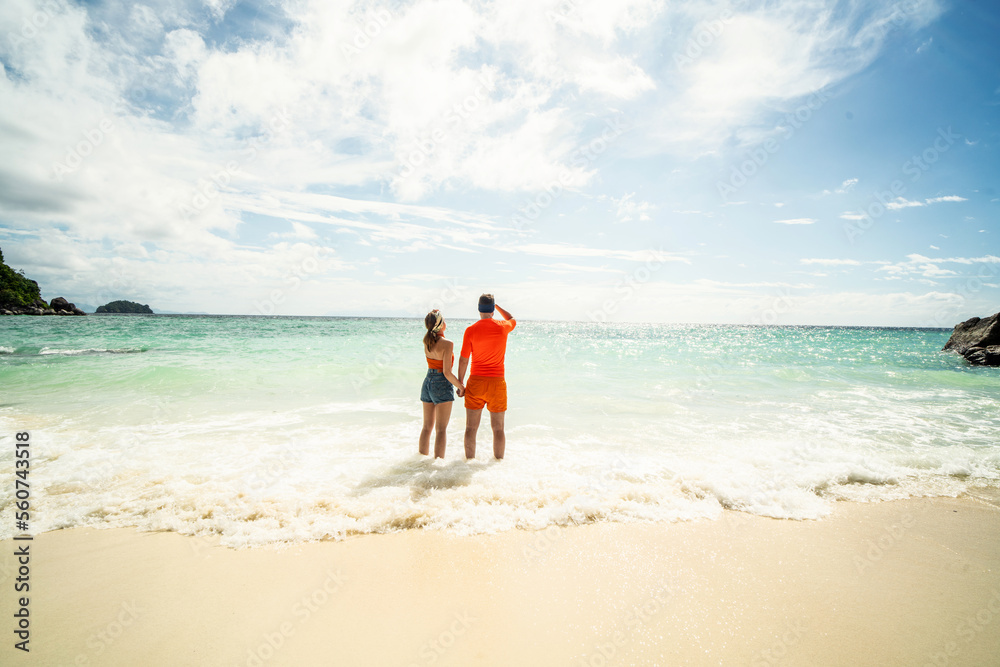 Beautiful couple walking together along the sea coast, looking at the sun. Back view. Tourism. Travel.