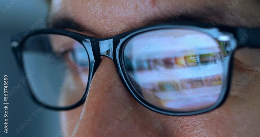 Close up male eyes in eyeglasses working late at night scrolling internet pages in front of laptop computer at home. Macro portrait of male in glasses with reflection of computer screen working online