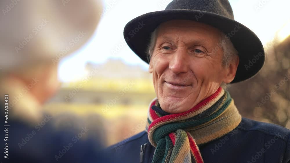 Close-up portrait of smiling loving senior Caucasian man talking looking at unrecognizable woman outdoors. Happy confident retiree dating with spouse on city street enjoying leisure Close-up portrait of smiling loving senior Caucasian man talking looking at unrecognizable woman outdoors. Happy confident retiree dating with spouse on city street enjoying leisure