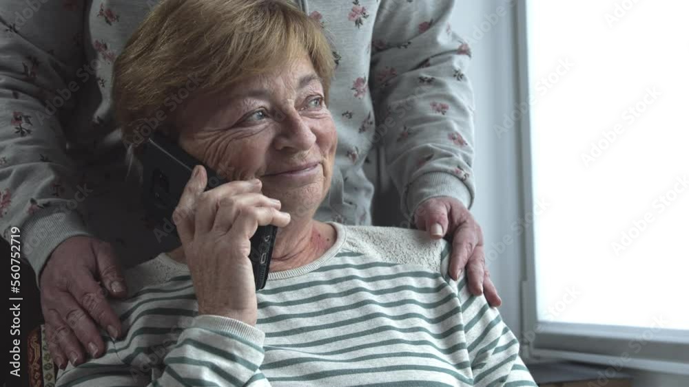 An elderly woman talking on the phone is upset and worried. Tears on eyes. Daughter supports her by hugging her shoulders. Family values and friendly support An elderly woman talking on the phone is upset and worried. Tears on eyes. Daughter supports her by hugging her shoulders. Family values and friendly support