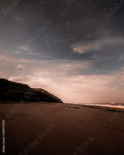 Dreamy landscape of empty beach at dawn with a long stretch of sand and rocky coast in the distance. Atmospheric mood with and vertical orientation. Quiaios, Portugal photo