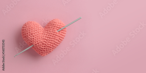 Crocheted amigurumi pink heart with crochet hook on a pink background. Valentine's day banner