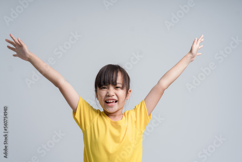 Happy little girl. Cheerful little girl keeping arms raised and smiling while standing isolated on white