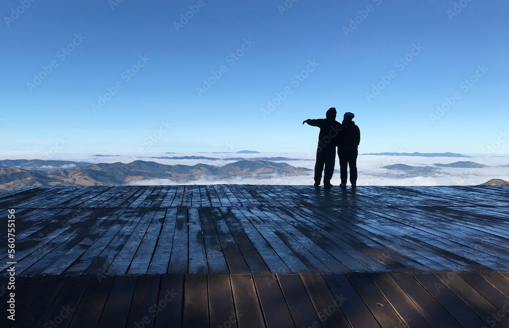 couple looking at the city from a beautiful view on a hang gliding ramp at the top of the serra da mantiqueira mountains with a blue sky over the clouds as the man points towards the horizon