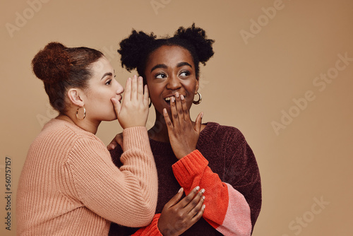 Friends, gossip and women share secret on studio background and product placement mockup. Secrets, rumor and surprise whisper in ear, black woman with happy woman discuss discount sale announcement