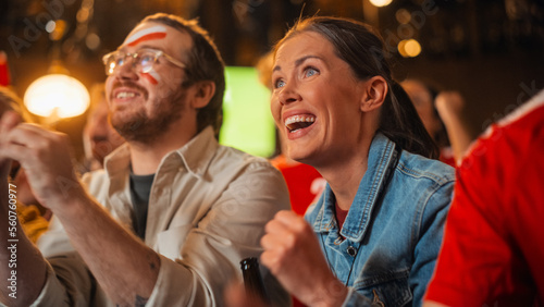 Young Soccer Fans Couple Watching a Live Football Match in a Sports Bar. Crowd with Colored Faces Cheering for Their Team. Player Scores a Goal and Crowd Celebrate Winning the Championship.