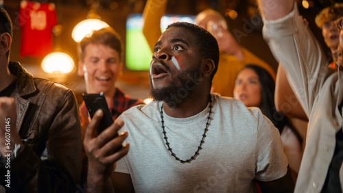 Portrait of an Excited Young Black Man Holding a Smartphone, Anxious About a Sports Bet on His Favorite Soccer Team. Lively Successful Emotions When Football Team Scores a Winning Goal. © Gorodenkoff
