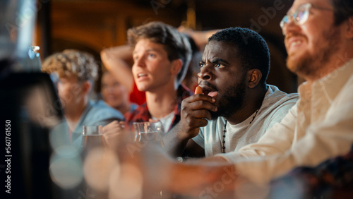Stressed African Man Watching a Live Soccer Match on TV in a Sports Bar. Excited Fans Cheering and Shouting. Young Black Male Nervous for His Team at Football World Cup.