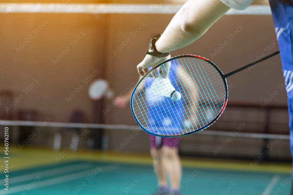 Badminton player holds racket and white cream shuttlecock in front of the net before serving it to another side of the court.	