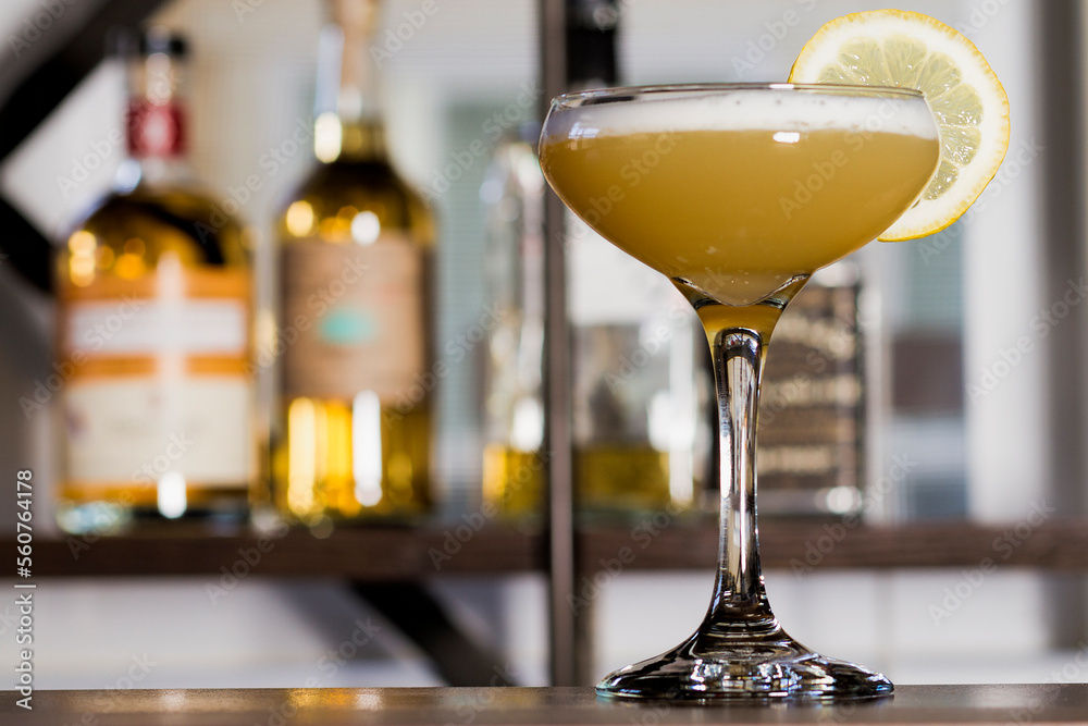 Traditional whiskey sour with a lemon wheel in front of liquor bottles