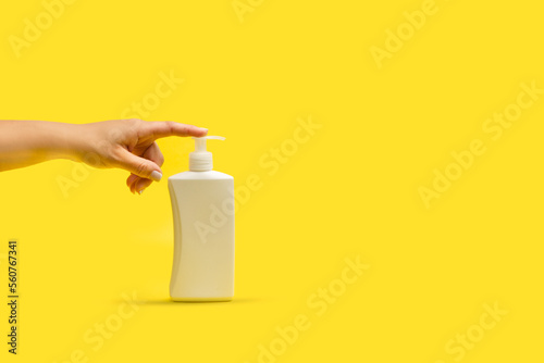 Mano de mujer apretando un bote dispensador de plástico blanco sobre un fondo amarillo brillante liso y asilado. Vista de frente y de cerca. Copy space photo