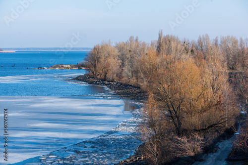 Ice drift on Dnieper river near Cherkasy city, Ukraine at sunny morning. The end of winter and the beginning of spring. Bare trees illuminated by rising sun