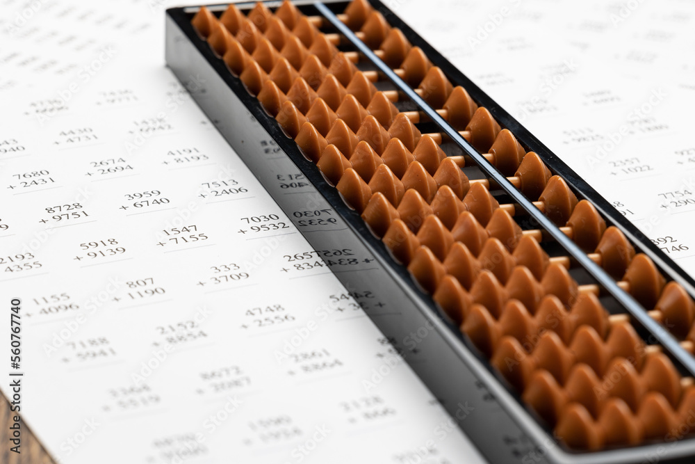 Japanese abacus soroban composed of an odd number of columns or rods, each having beads. It is placed on printed practice sheet for calculations of addition and multiplication Japanese abacus soroban composed of an odd number of columns or rods, each having beads. It is placed on printed practice sheet for calculations of addition and multiplication