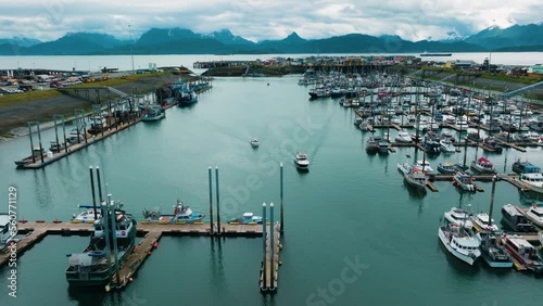 Aerial drone pull away of halibut Fishing boats pulling into marina and docking in small town Homer Alaska with beautiful mountain range backdrop