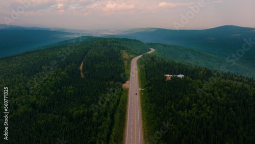 Aerial drone flyover 2 lane highway in the middle of nowhere Montana with lush green trees and mountains in the background at sunset