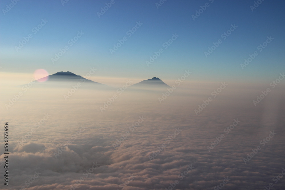 Background photo of low clouds in a mountain valley, vibrant blue sky. Sunrise or sunset view of mountains and peaks peaking through clouds.