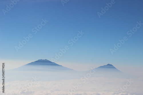 Background photo of low clouds in a mountain valley, vibrant blue sky. Sunrise or sunset view of mountains and peaks peaking through clouds.