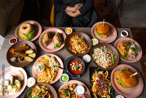 Top view photo of woman sitting at table full of delicious food in plates. Fries, soup, salad, burgers, sauces on festive dinner. Food, many dishes, menu of restaurant, beautiful serving food