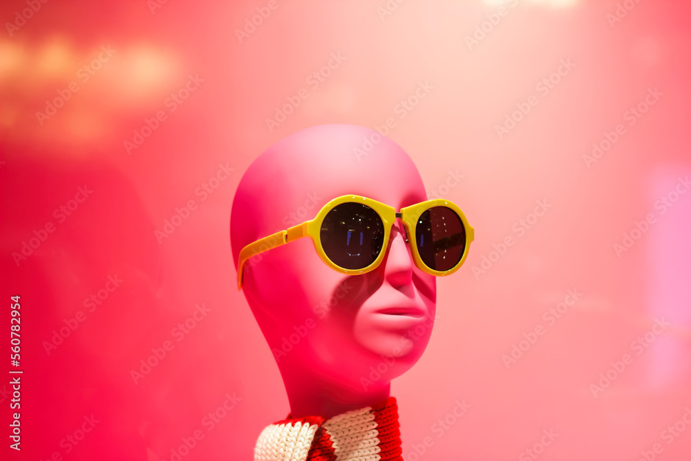 Fototapeta premium a pink display with a pink mannequin head in sunglasses and stripe scarf close up, pink wall on background