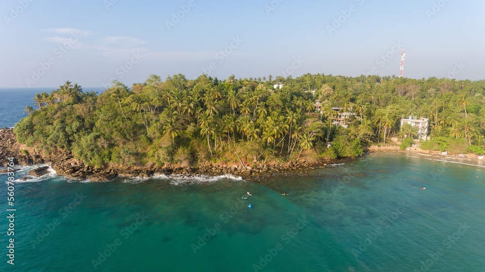 Aerial view of turquoise water of Pacific Ocean, Sri Lanka. A group of surfers are waiting for the waves from above. Beautiful destination for surfing at Hiriketiya Beach