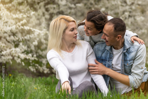 Happy family outdoors spending time together. Father, mother and daughter are having fun on a green floral grass. © Angelov