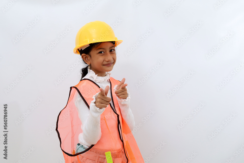 Adorable Asian little girl in the construction helmet as an engineer standing with pointing at the camera. Isolated on white