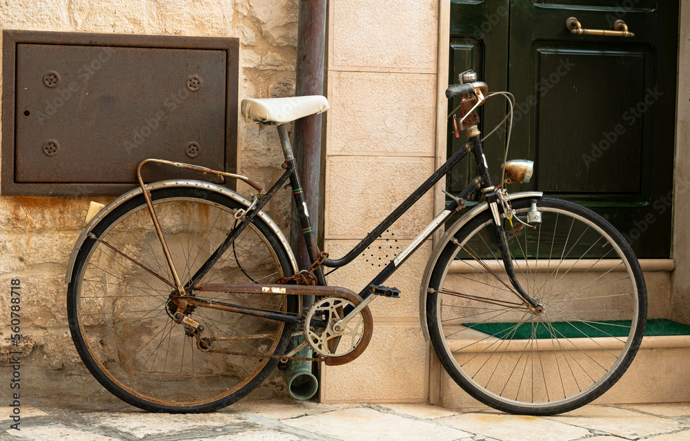 A vintage bicycle, cover with rust secure by the downspout near a home entrance in Italy, Bari. Nice old bike used by locals. Retro bike near a door.