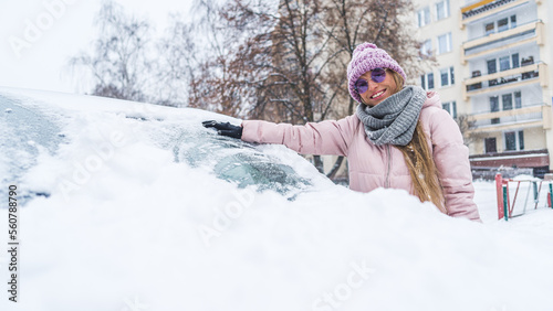 Young smiling woman cleaning first snow from the windshield of her car . High quality photo