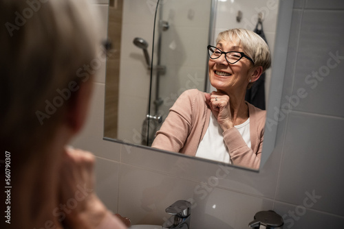 Confident senior woman looking at her reflection in the mirror and talk to himself. Trying to rise self-esteem and motivate himself.
