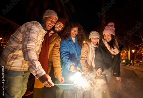 Group of friends celebrating with sparklers fireworks at night party. Diverse people with different ethnicity having fun together - Winter Holidays lifestyle concept