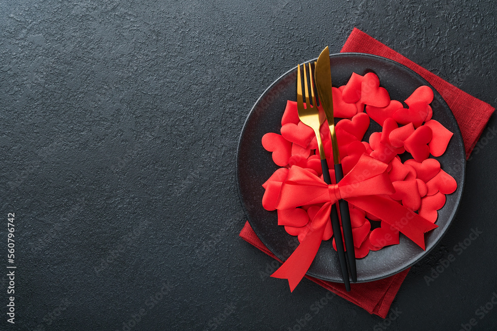 Valentines day romantic table setting. Empty or closeup of a dinner black plate, knife, fork and decorative silk hearts on black background. Holiday concept. Copy space for inscriptions. - obrazy, fototapety, plakaty 