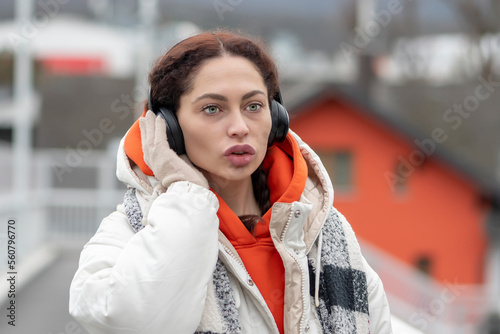 An emotional portrait of a woman 25-30 years old, listening to music in Bluetooth headphones on a blurry urban background.