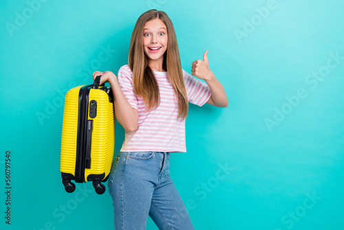 Portrait of excited positive girl hold suitcase demonstrate thumb up feedback isolated on teal color background