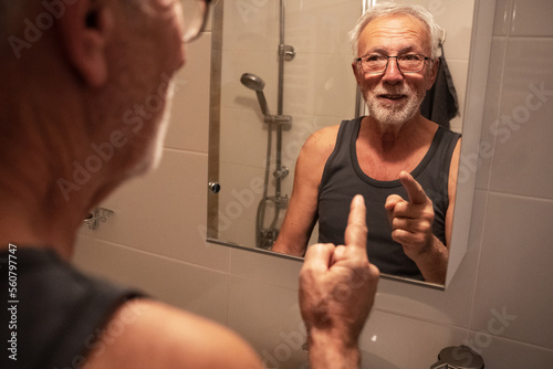 Confident senior man looking at his reflection in the mirror and talk to himself. Trying to rise self-esteem and encourages himself.