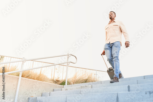 Handsome young black man carrying a suitcase going down the stairs. Think big and success concept. Skyscrapers blurred background.