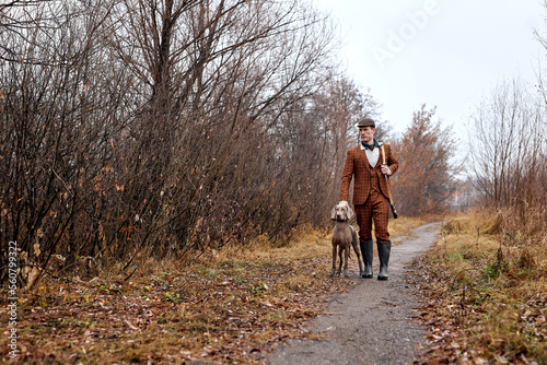 confident Male hunter with nice hunting dog Weimaraner, portrait in rural area during hunting season, handsome caucasian guy in brown suit, walking together, going in forest. hunting, wildlife