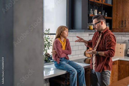 Upset father having a serious conversation with his young stubborn daughter  gesturing with hands  arguing. Girl is sitting with the arms crossed and looking at him.