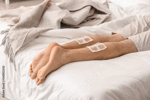 Ill man with mustard plasters on his legs lying in bedroom, closeup