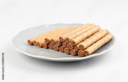 Plate with heap of tasty wafer rolls on grey background