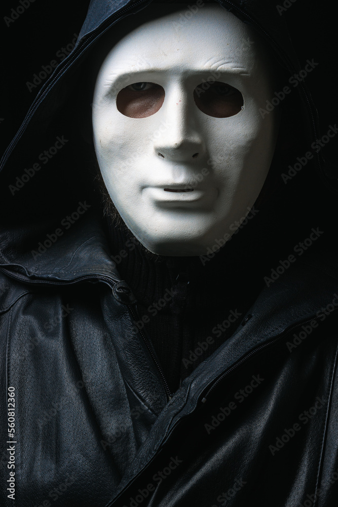 Man in terrible face mask staring at camera against dark background cloak with hood Man in terrible face mask staring at camera against dark background cloak with hood
