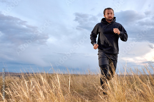 Handsome Young Caucasian Male Jogging Through the field. Man Wearing Black sportive wear. athlete guy with beard is motivated to be muscular, strong, in perfect physical shape. sport, fitness © alfa27