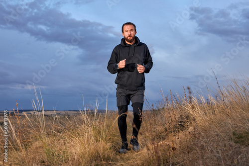 Jogger Young Caucasian Male Running Through the field. Man Wearing Black sportive wear. athlete guy with beard is motivated to be muscular, strong, in perfect physical shape. sport, fitness © alfa27