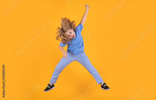 Funny boy jumping in air. Kid boy jump fly movement wear shirt and jeans isolated on yellow studio background.