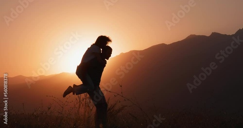 Silhouette view of a man spinning a woman on his back at sunset. A romantic date and love on nature of loving happy couple. 4k slowmotion