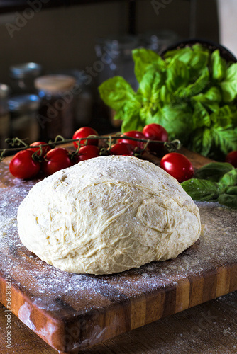 Fresh handmade pizza dough on a wood board with organic tomatoes and basil