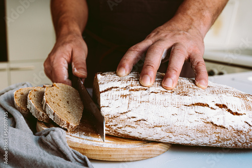 male baker at home kitchen cutting bread