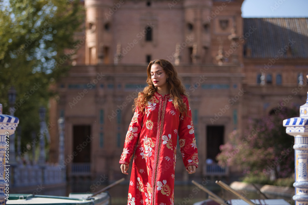 Beautiful young woman in a typical Moroccan red suit, embroidered with gold and silver threads, posing next to the boats in the Spanish square. Concept beauty, ethnicity, typical suits, Arab.