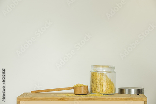 Still life with an open glass jar filled with pasta for soup with a wooden ladle and stainless steel lid