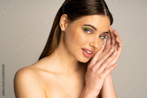 Smiling teen model with colorful makeup posing and looking at camera isolated on grey.